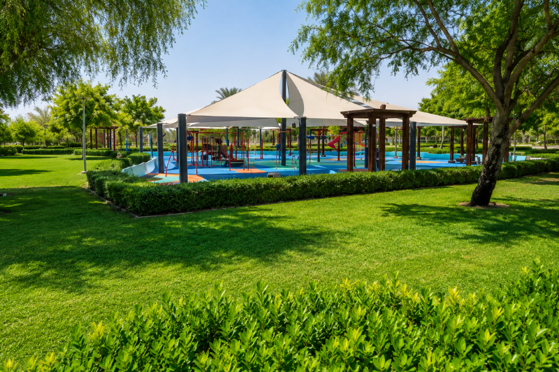 Shaded playground surrounded by green lawns at Al Quoz Pond Park in Dubai