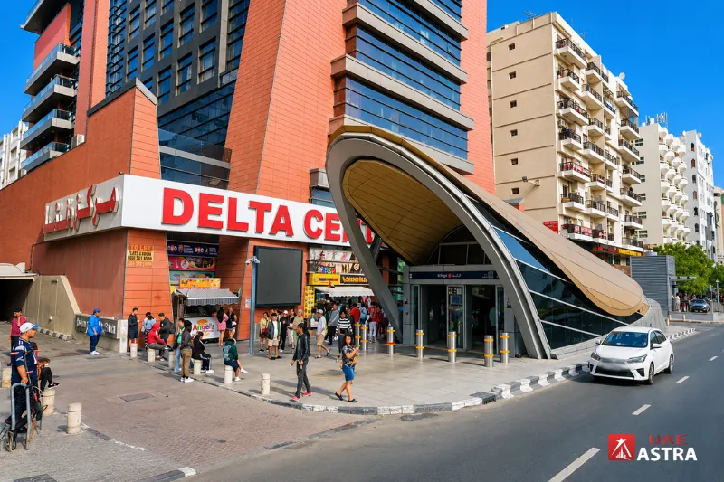 Street view of Al Rigga Metro Station entrance surrounded by hotels, shops, and commercial buildings in Deira, Dubai