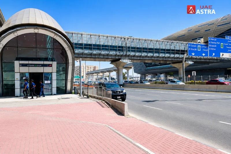 Exterior entrance of Al Qiyadah Metro Station with pedestrian bridge and directional road signs in Dubai
